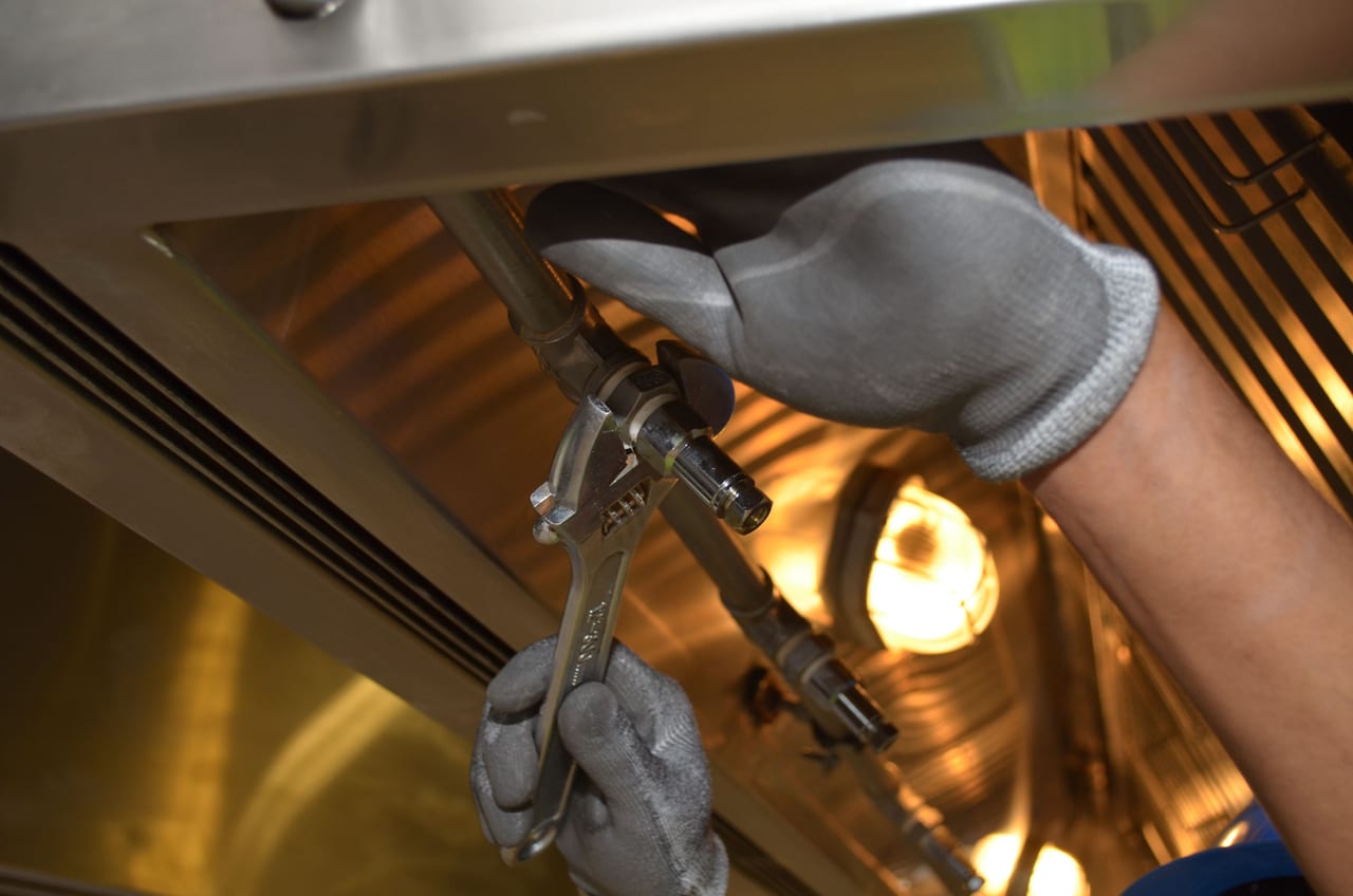 Gloved hands using a wrench on plumbing beneath a sink